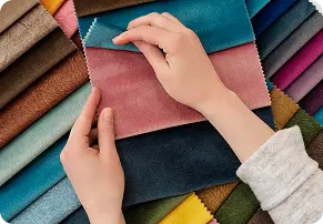 Mani con campioni di velluto rosa antico e blu su sfondo di campionari tessili colorati.