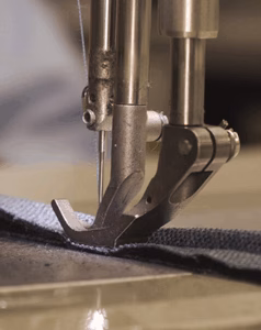 Close-up of a double-needle industrial sewing machine stitching dark fabric
