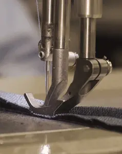 Close-up of a double-needle industrial sewing machine stitching dark fabric