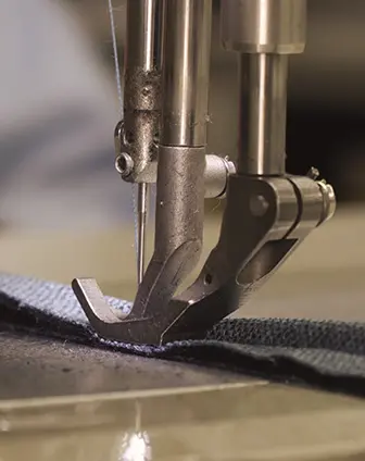 Close-up of a double-needle industrial sewing machine stitching dark fabric