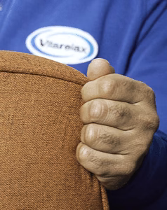 Hand gripping a brown upholstered cushion with a Vitarelax logo in the background