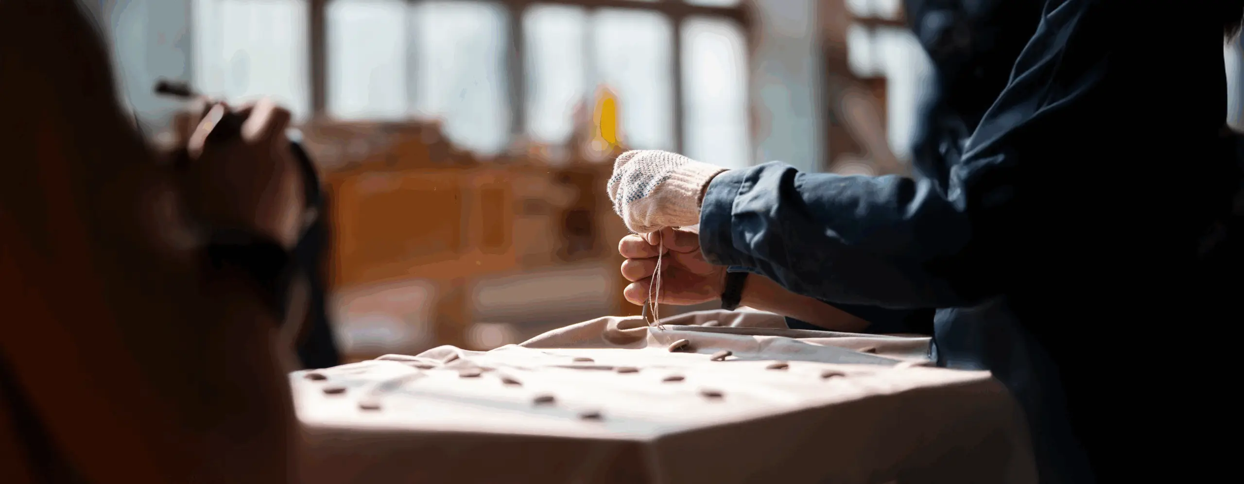 Artisan hands sewing buttons on fabric in a bright workshop
