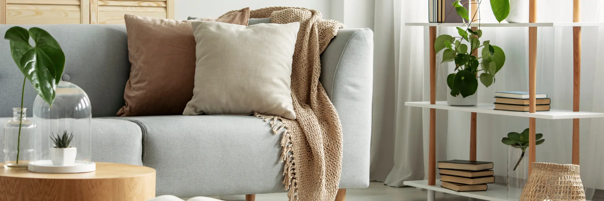Modern grey sofa with beige cushions and a knitted blanket in a bright living room